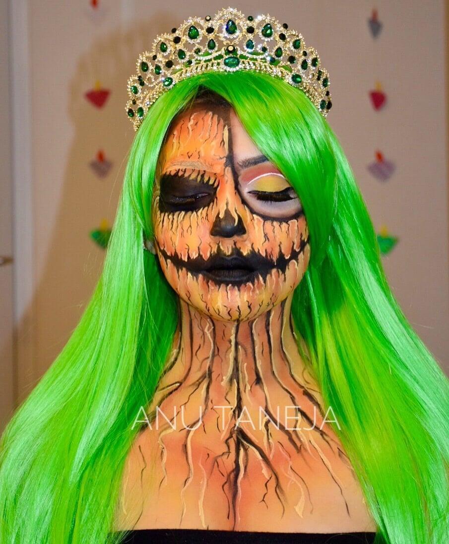 Portrait of a model wearing a neon green wig and jeweled crown, with dramatic pumpkin-inspired fantasy makeup featuring black hollow eyes, cracked orange face and body paint, and dark painted lips.